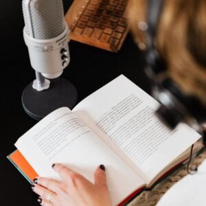 Person with headphones on reading and narrating a book into a microphone