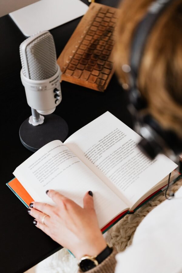 Person with headphones on reading and narrating a book into a microphone